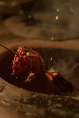 Close-up of a flaming tandoor oven with skewers of marinated chicken glowing over the fire.