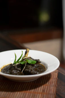 A close-up of a steaming bowl of traditional Bangladeshi khichuri garnished with fried eggplant and fresh coriander.
