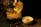 A vibrant dish featuring biryani served in a round bread bowl. A piece of cooked chicken with onion rings and garnishes is placed on top. A papadum is balanced upright, adding a crispy element. A small bowl of yogurt with herbs and spices is beside it, all set on a dark, textured surface.