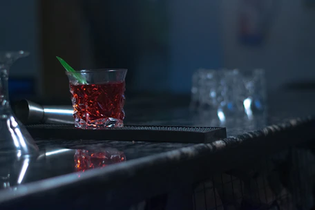 A moody, dimly lit bar counter showcasing a vintage genever bottle beside a classic cocktail glass with a rich amber drink.