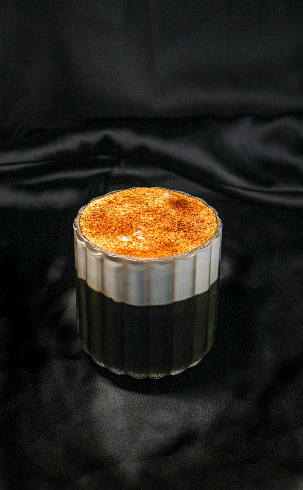 a cake in a glass container on a black cloth