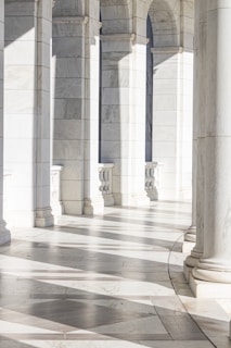 Elegant marble arches cast intricate shadows on the smooth tiled floor, creating a serene and sophisticated pattern. The space appears bright and open, with natural light enhancing the architectural details.