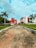 A modern building with a bold red and white facade is surrounded by palm trees and manicured lawns. The sky is lightly clouded, and the wide pathway leading to the building suggests an institutional or corporate setting.
