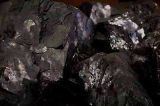 A collection of dark, metallic minerals with shiny surfaces and various angular fragments. The texture appears rough with a mix of reflective and matte areas.