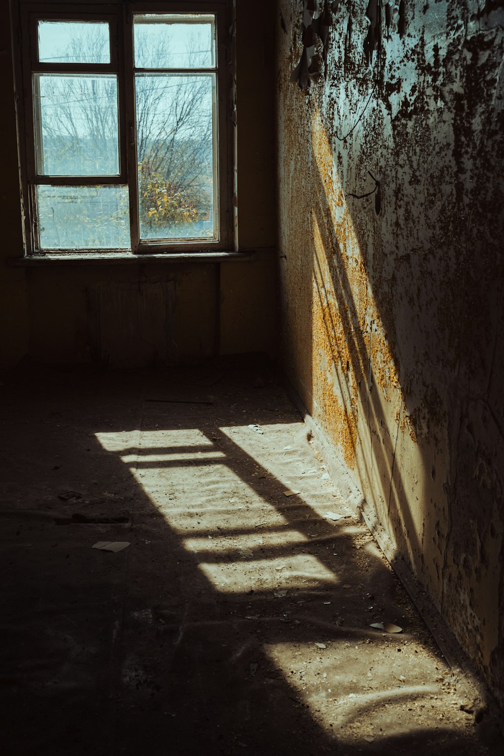 an empty room with a window and peeling paint