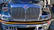 A close-up of a semi-truck’s polished silver grille reflecting the highway ahead.
