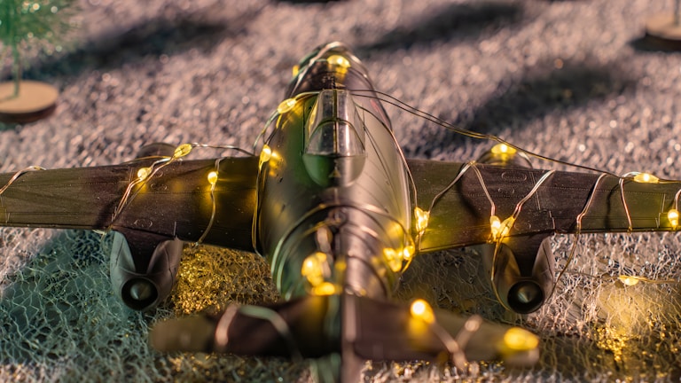 A model airplane wrapped in yellow fairy lights rests on a textured surface, creating a festive and whimsical atmosphere.
