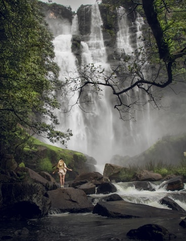 a woman standing on a rock in front of a waterfall
