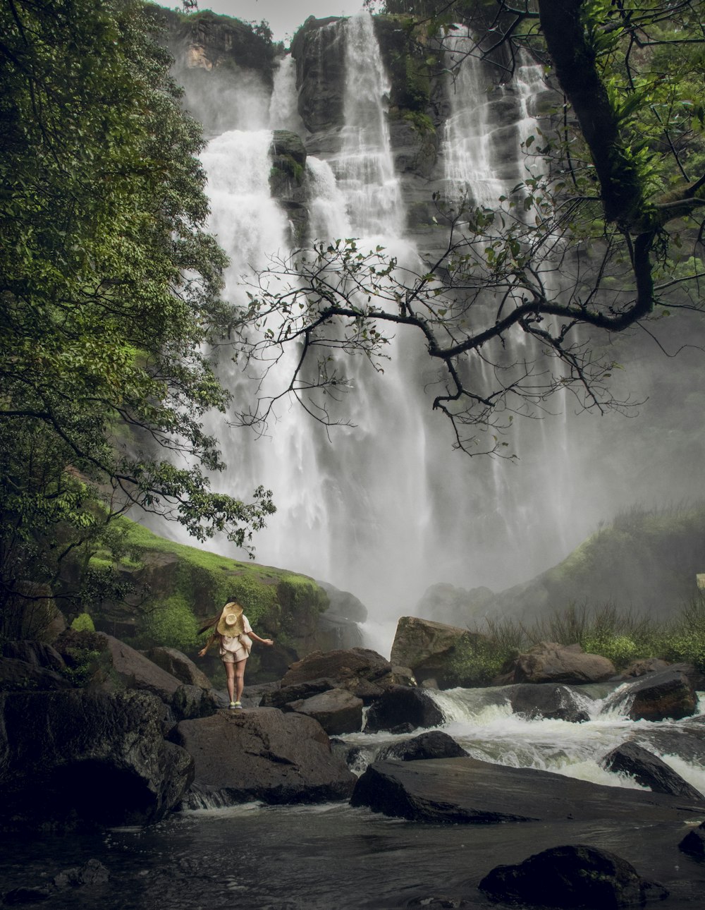 a woman standing on a rock in front of a waterfall