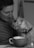 A person with a gentle smile leans towards a small, fluffy dog, creating an intimate and warm moment. They appear to be sharing a close connection. In the foreground, there is a cup, possibly suggesting a cozy setting.