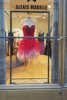 A vibrant red dress displayed on a mannequin against a soft beige background, highlighting its fine fabric texture.