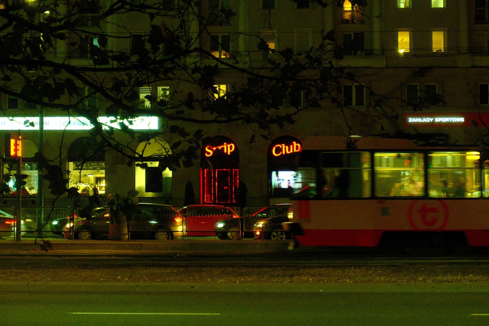 a red and white bus driving down a street at night