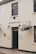 A white brick building with the sign 'RESTAURANT & BAR' above a black door. Hanging baskets with flowers are mounted on either side of the entrance. Two lantern-style lights are affixed to the wall near the door. The building has a traditional appearance with quaint, decorative touches.