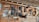 A wooden wall displays an assortment of traditional masks and handcrafted items. Several masks with expressive faces are arranged alongside woven gourds and decorative objects, including a wooden fish sculpture and an ornamental fan. The design reflects a rustic, cultural collection.