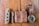 A rustic wooden surface features a collection of everyday carry items. A folding knife with a textured handle, a compact brown pocket tool, a leather pouch embossed with 'Strong Cow,' and a stylish wristwatch with a brown leather strap are neatly arranged in a row.