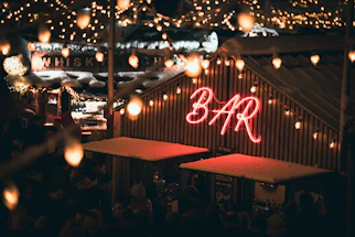 A cozy mobile bar setup glowing warmly under string lights at an outdoor evening event.