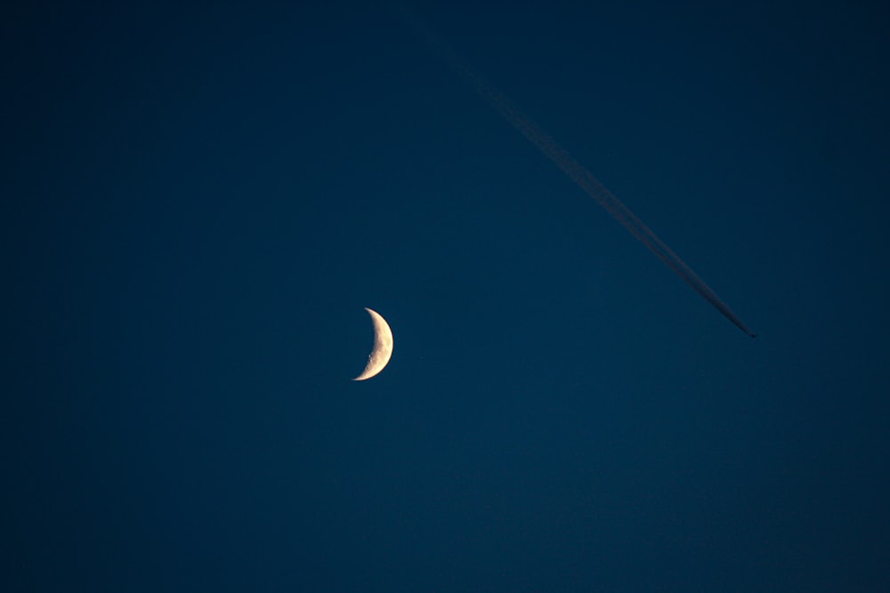 a plane flying in the sky next to a half moon
