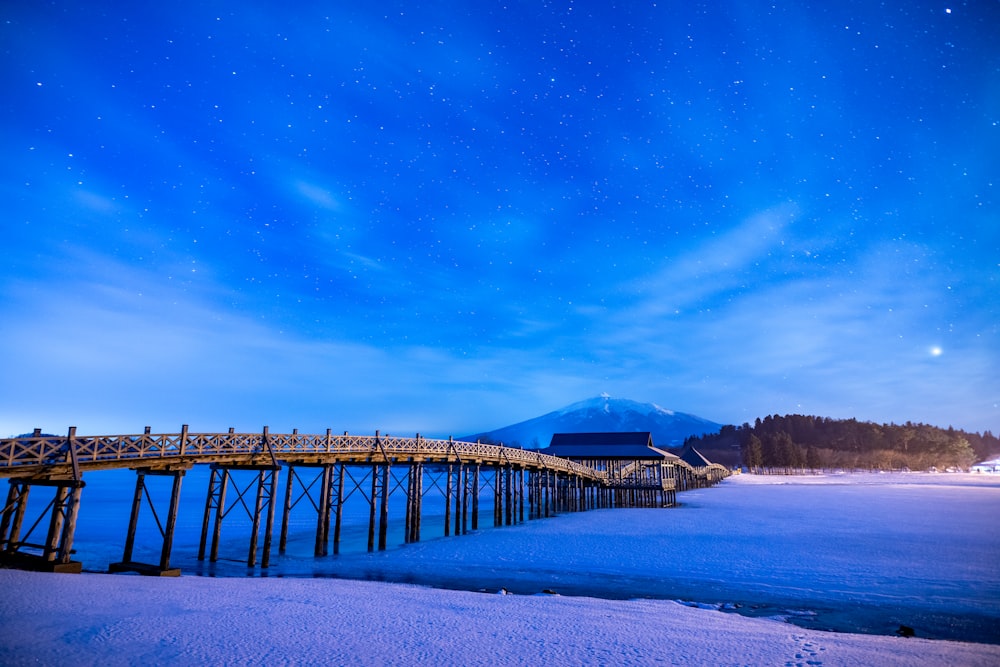 a long wooden bridge over a body of water under a night sky