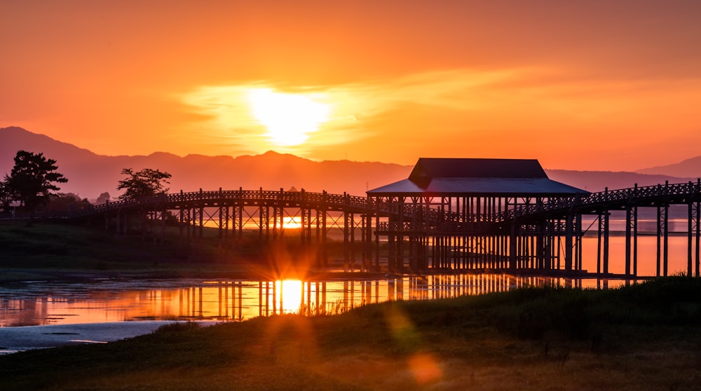 the sun is setting over the water with a bridge in the foreground