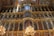 A richly decorated, multi-tiered iconostasis adorned with numerous religious paintings and ornate gold detailing. Brightly lit chandeliers cast a warm glow across the opulent structure, which features a combination of biblical figures and intricate carvings.