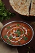 a bowl of red curry with pita bread in the background
