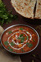 Freshly baked naan bread beside a bowl of creamy curry with vibrant spices.