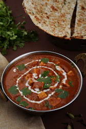 A warm bowl of creamy paneer butter masala with a side of naan bread.