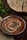 A bowl of rich, creamy paneer curry garnished with coriander leaves and a swirl of cream sits on a table. Beside it, there is a naan bread, partially sliced and garnished with herbs. Fresh cilantro leaves are placed on the table, adding a touch of green to the scene.