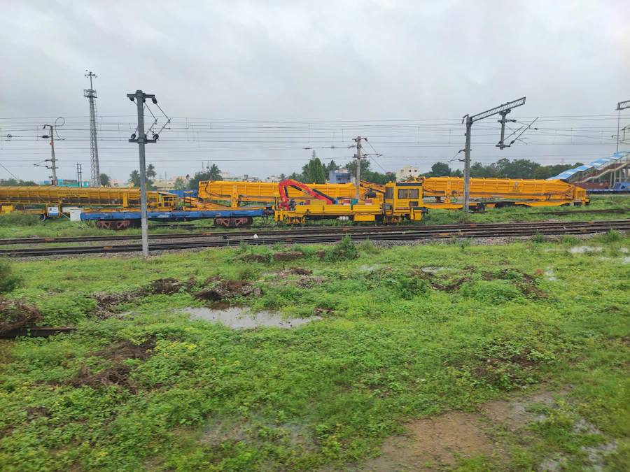 A railway yard with several tracks, overhead power lines and yellow maintenance vehicles.