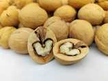 A close-up view of several walnuts with two prominently displayed in the center. One walnut is open, revealing the recognizable brain-like shape of the nut inside, while the others are uncracked and serve as the background.