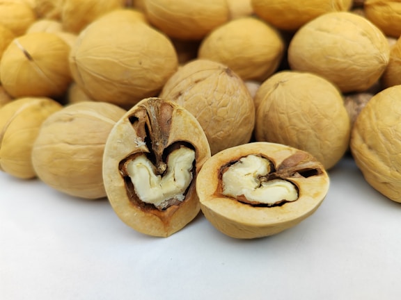A close-up view of several walnuts with two prominently displayed in the center. One walnut is open, revealing the recognizable brain-like shape of the nut inside, while the others are uncracked and serve as the background.