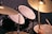 A close-up view of a drum set with a focus on the top cymbals and drum heads. A hand is visible holding a drumstick, implying that the person is playing or about to play. The drums have a black finish, and there is an emphasis on texture and lighting that highlights the metallic sheen of the cymbals.