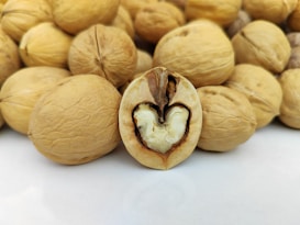A collection of walnuts with one prominently displayed in the foreground, showcasing the inside of a split walnut revealing the nut and intricate shell detail.