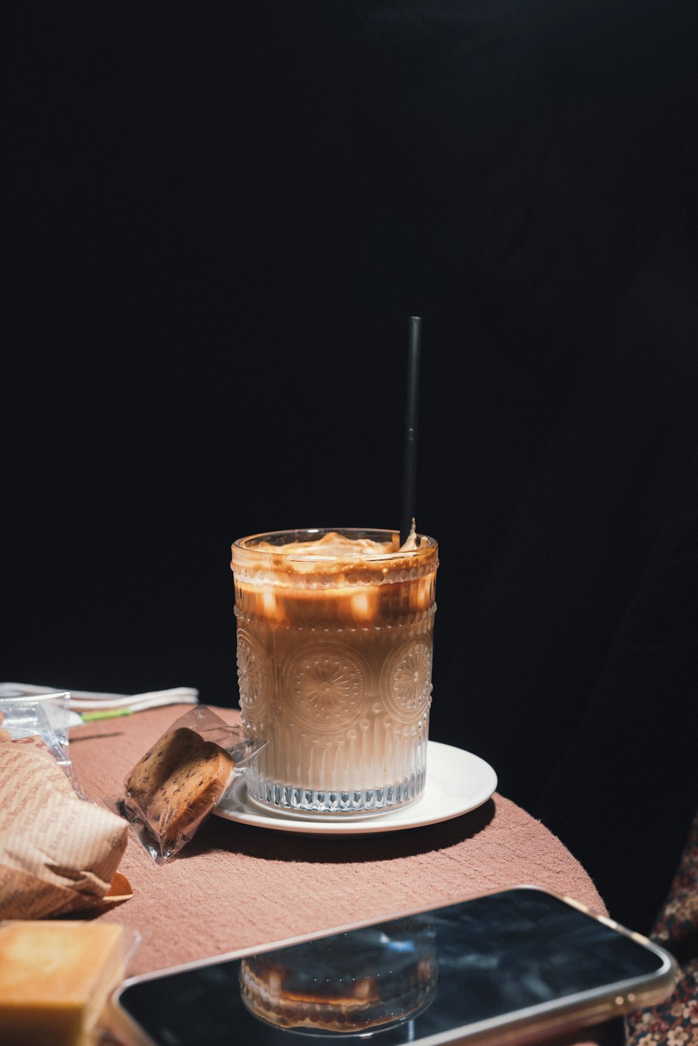 a glass of iced coffee on a table with a cell phone