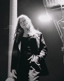 Black and white street portrait of a stylish person framed by urban architecture and soft shadows.