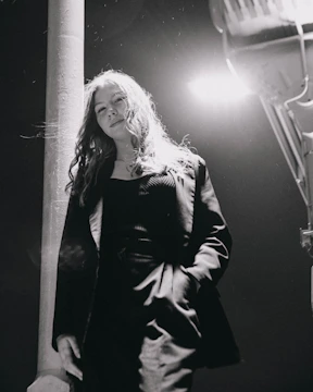 Black and white street portrait of a stylish person framed by urban architecture and soft shadows.