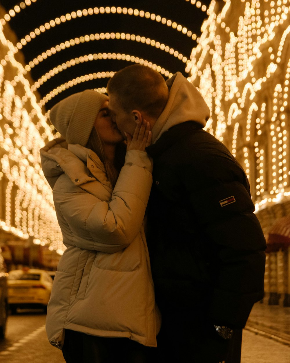 a man and woman kissing in front of christmas lights