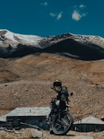 A motorbike parked beside a winding hill road with snow-capped peaks in the background.