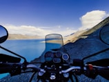 A motorcycle parked beside a scenic lake with mountains in the background.