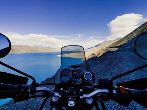 A serene roadside view capturing a motorcycle parked beside a winding mountain path under a clear blue sky.