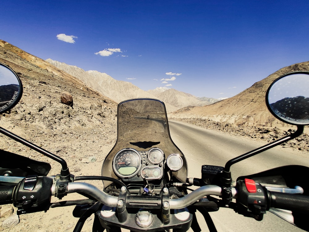 a motorcycle driving down a desert road with mountains in the background