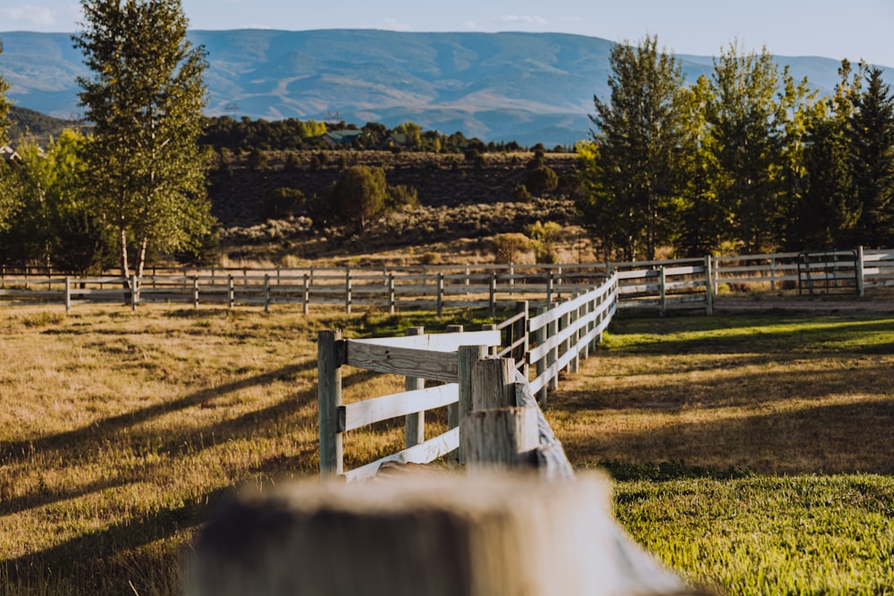 a wooden fence in a field with mountains in the background