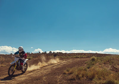 A rugged dirt bike kicking up dust on a forest trail under a bright blue sky
