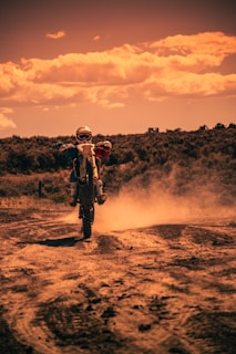 A rider performing a wheelie on a dirt track, dust rising behind the bike.
