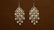 Two intricately designed chandelier earrings feature multiple white pearls set in a gold frame against a plain brown background.