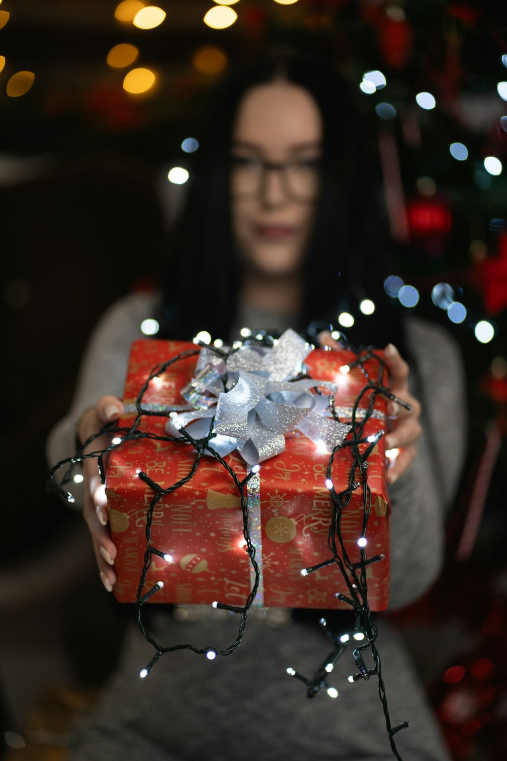 a woman holding a wrapped present in front of a christmas tree