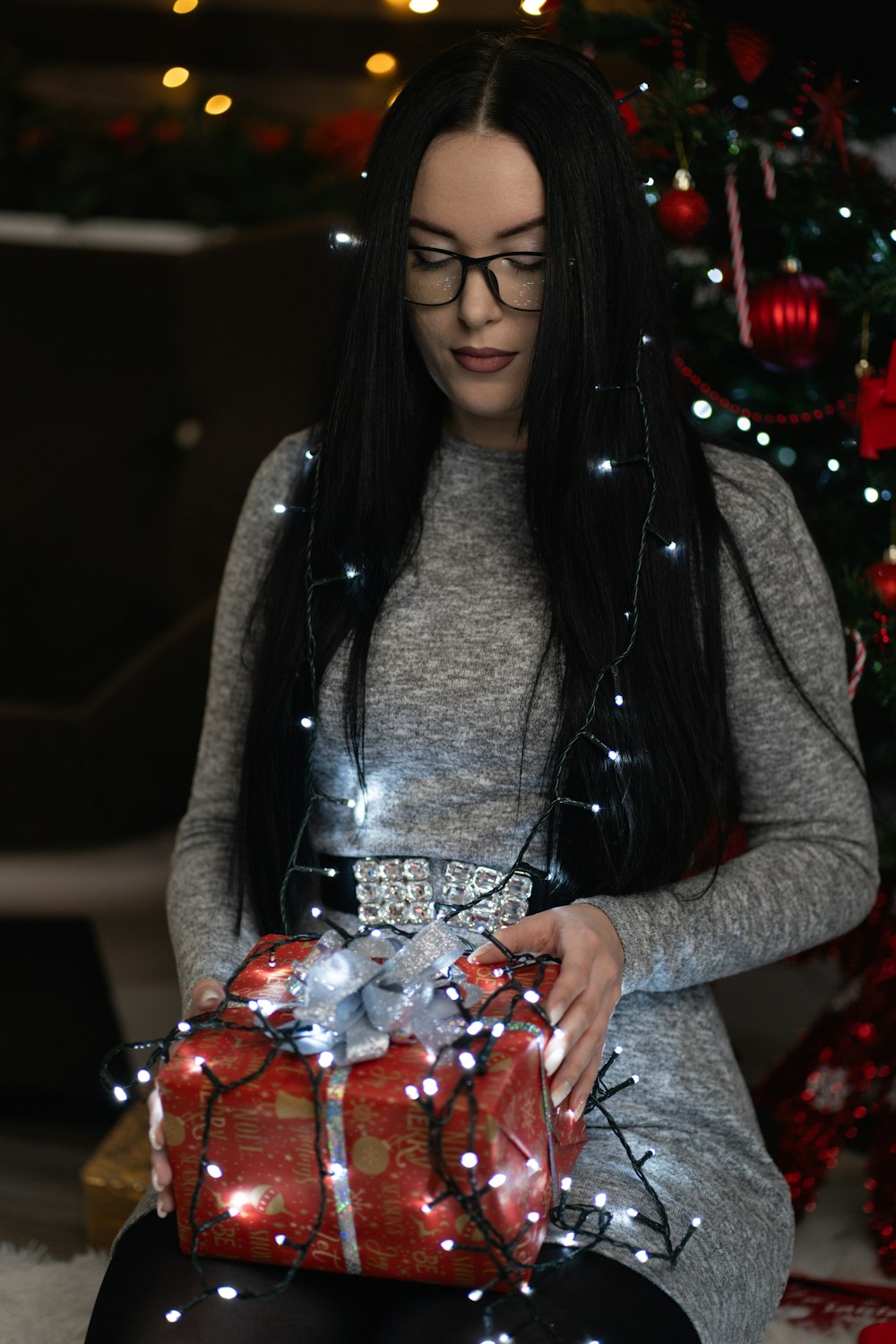 a woman sitting in front of a christmas tree holding a present