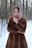 A woman wearing a stylish winter coat, standing in a snowy park with trees in the background.