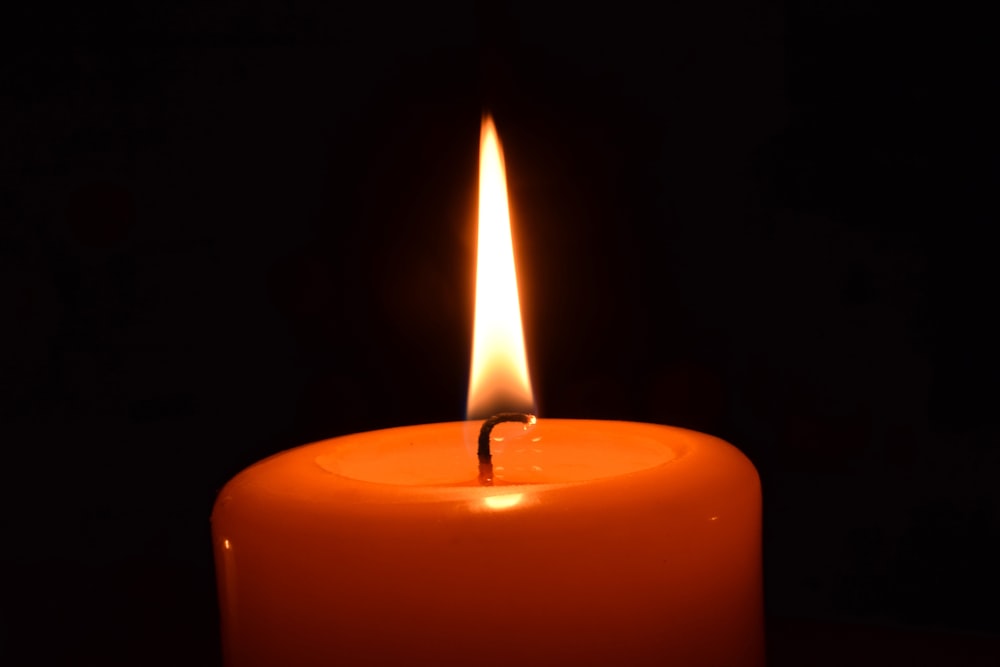 a lit candle in the dark with a black background