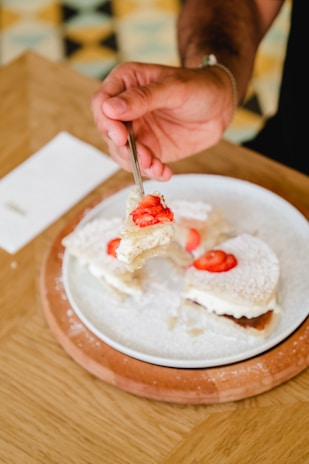 A hand holding a pistachio-topped strawberry dessert, ready to enjoy.